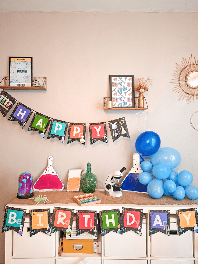 Décoration d’anniversaire scientifique avec fioles en carton et ballons créant une atmosphère de laboratoire.